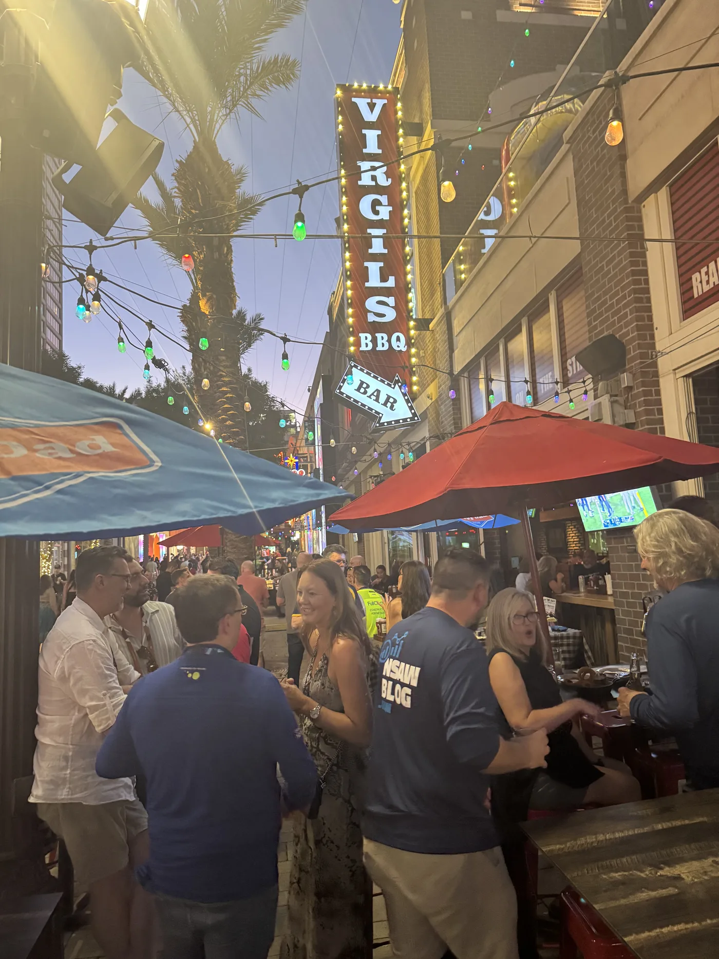 The evening crowd under string lights with the Virgil's BBQ sign glowing at dusk
